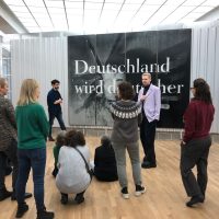 Day 4 – Hamburger Banhof 1 People meeting in a room next to a poster